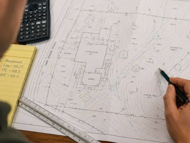 Topographic survey map review on desk | Jacksonville Land Surveying Homeowner reviewing a printed topographic survey with contour lines and elevation markings on a desk